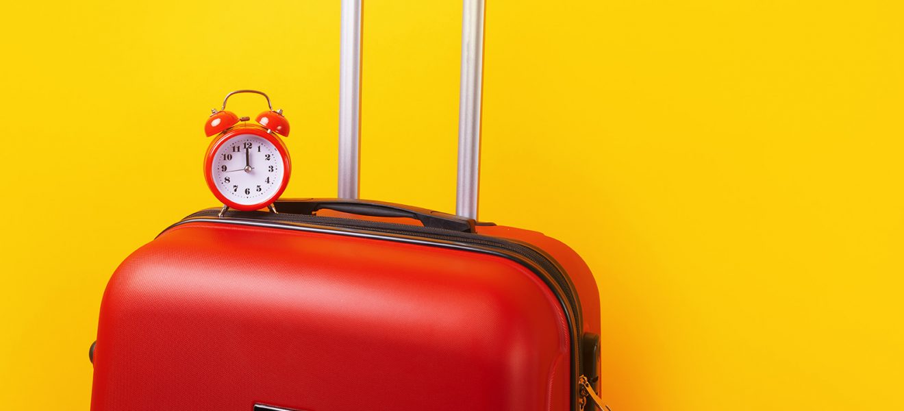 Travel case with alarm clock  over yellow background. Time to voyage. Voyage concept. Retro alarm clock with red suitcase, panoramic mock-up