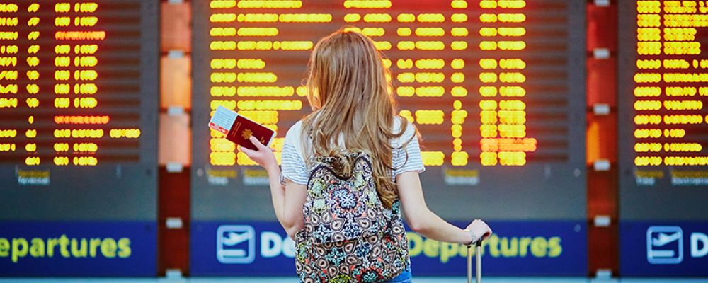 Tourist Girl With Backpack And Carry On Luggage In International Beautiful young tourist girl with backpack and carry on luggage in international airport near flight information board