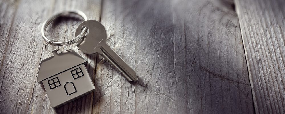 House key on a house shaped keychain resting on wooden floorboar House key on a house shaped keychain resting on wooden floorboards concept for real estate, moving home or renting property
