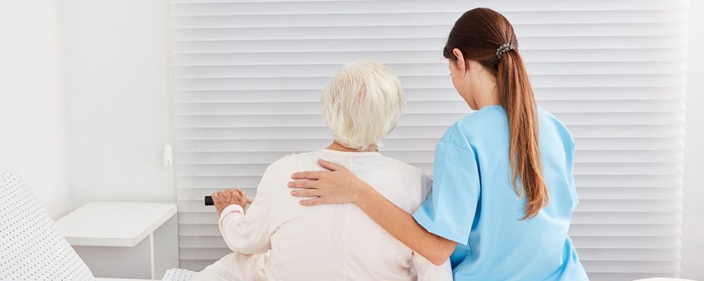 A frail old elderly woman as a patient gets help getting out of bed